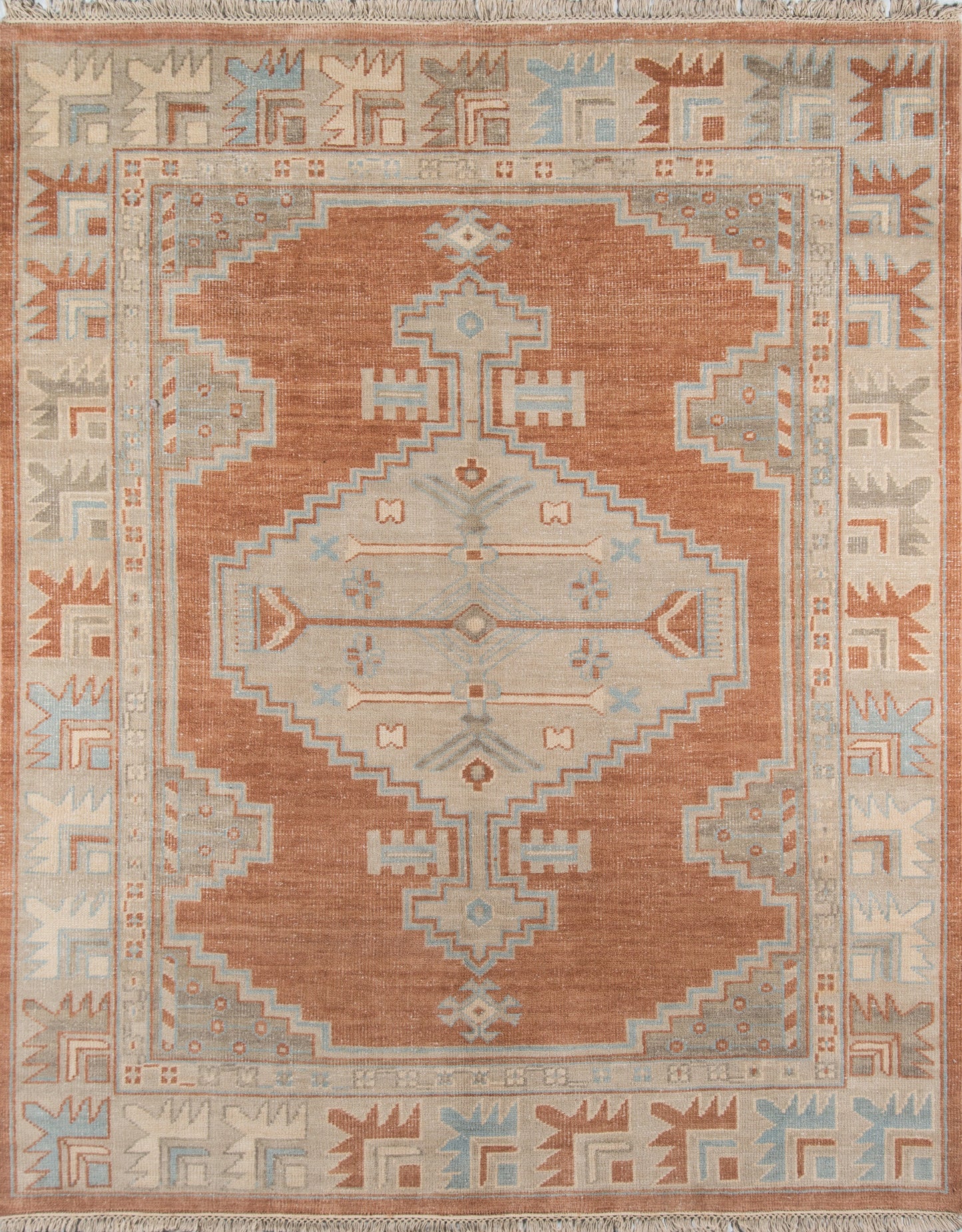 Rust-orange kilim-style area rug with pale blue and ivory geometric medallion, fringed ends; ideal for living room decor.