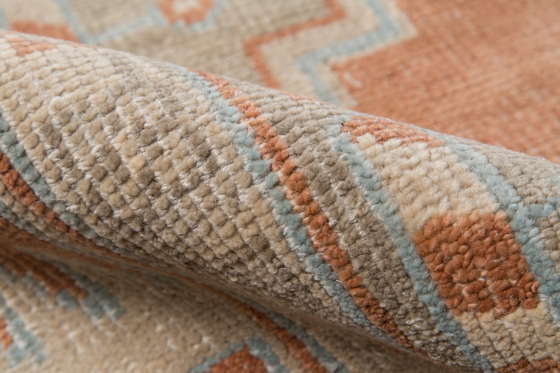 Close-up of a plush beige rug with rust orange and pale blue geometric motifs and thick textured pile.