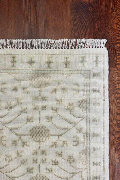 Cream cotton rug with grey-green floral pattern and fringed ends; rectangular, traditional oriental style.