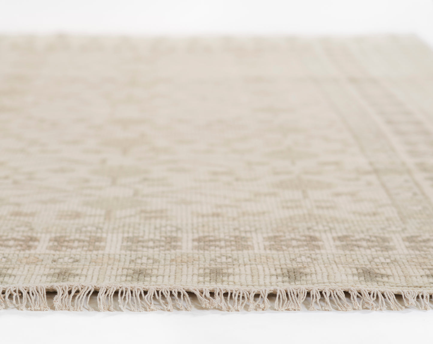 Beige woven area rug with fringed edge and subtle geometric texture.