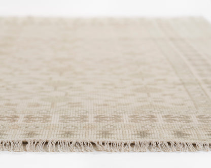 Beige woven area rug with fringed edge and subtle geometric texture.