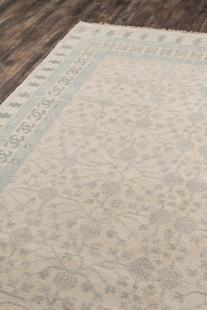 Ivory area rug with pale blue border and subtle floral pattern; fringed edges on wood floor.