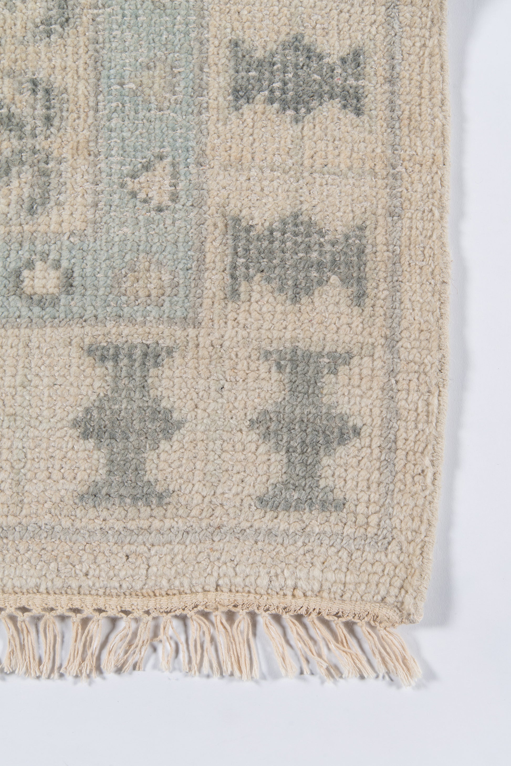 Beige rug with light blue-gray geometric diamonds, soft pile, fringed edge.