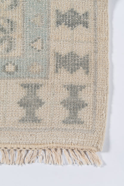 Beige rug with light blue-gray geometric diamonds, soft pile, fringed edge.