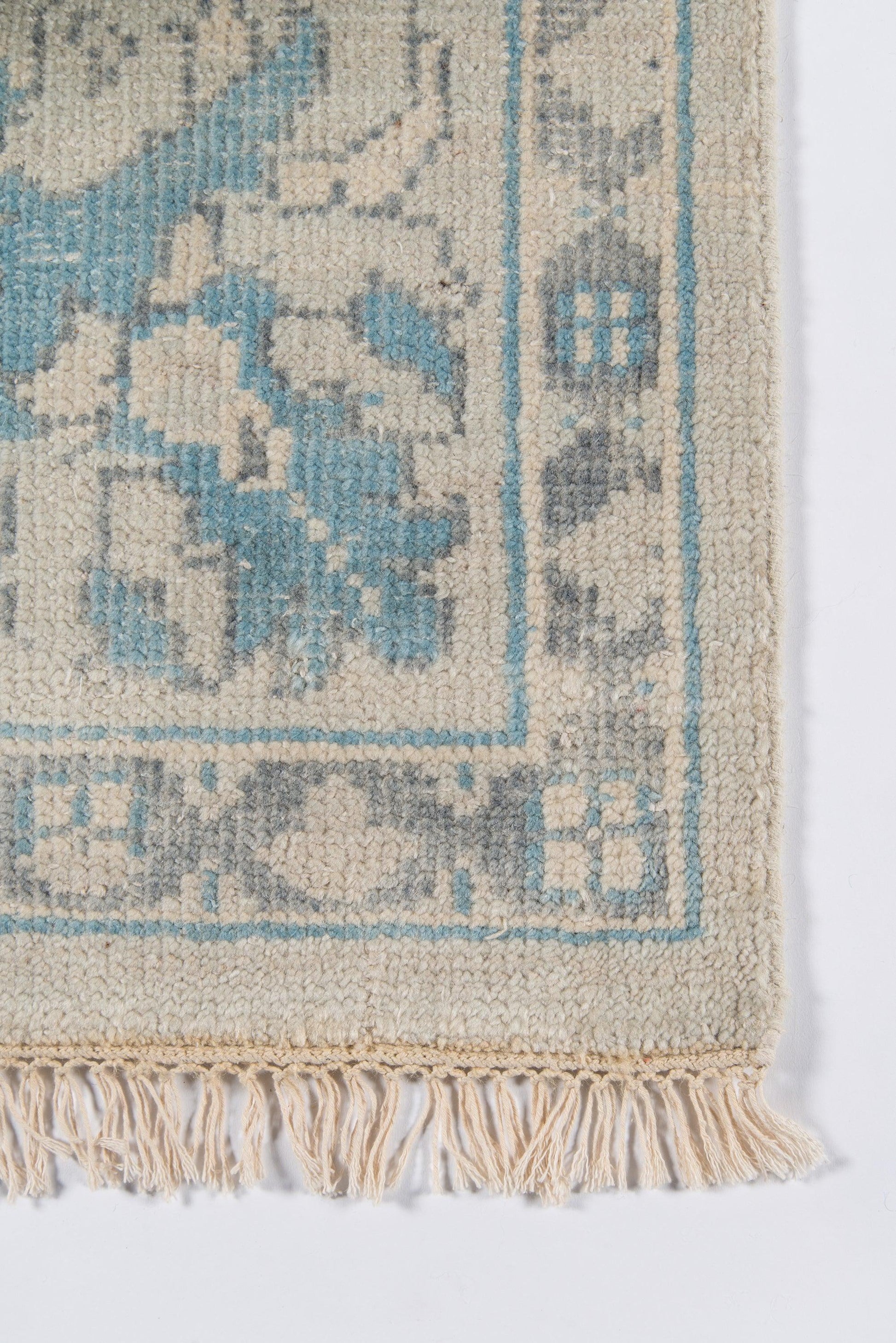 Cream woven rug with light blue floral motif, blue border, and fringe tassels.