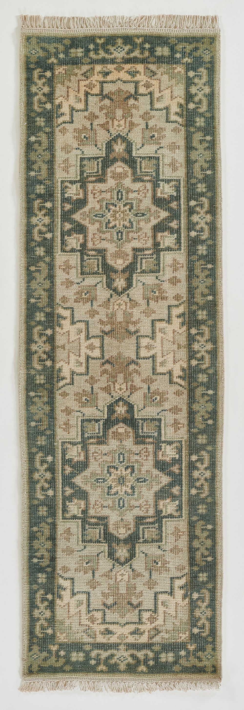 Long rectangular oriental rug runner with cream field, muted sage green border, geometric central medallion and fringed ends.