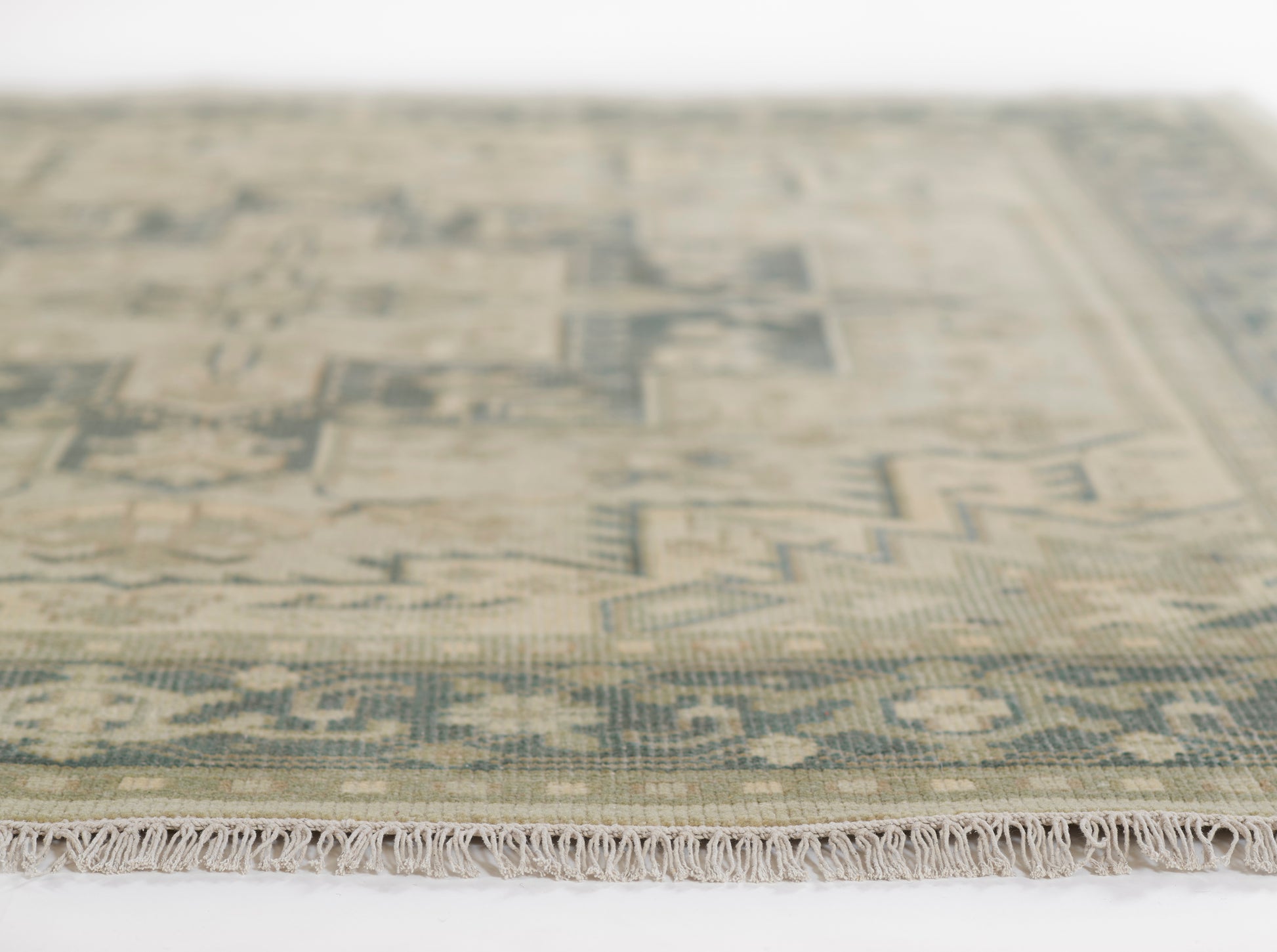Sage green oriental rug with faded ivory geometric motifs and fringed edge.