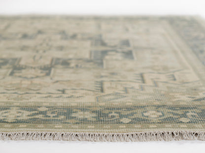 Sage green oriental rug with faded ivory geometric motifs and fringed edge.