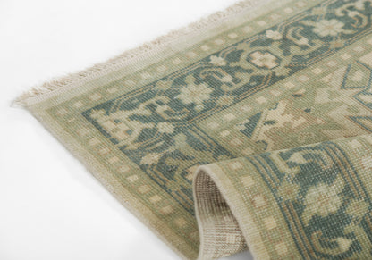 Woven wool area rug with fringed edge in green, teal and beige geometric medallion pattern; folded to show underside.