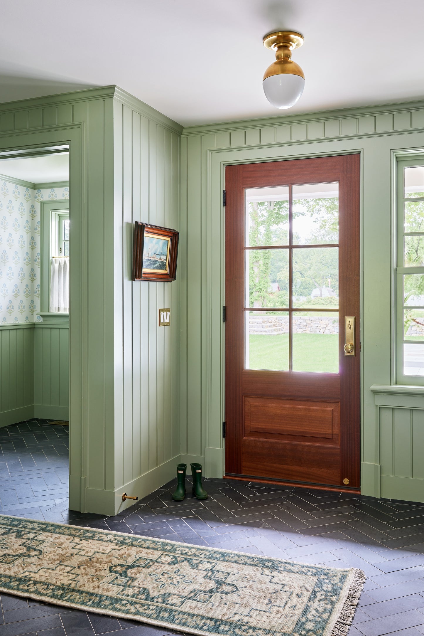 2'6" x 8' green patterned runner rug in an entryway with mint-green beadboard walls, dark herringbone floor, and a wooden front door with brass hardware.
