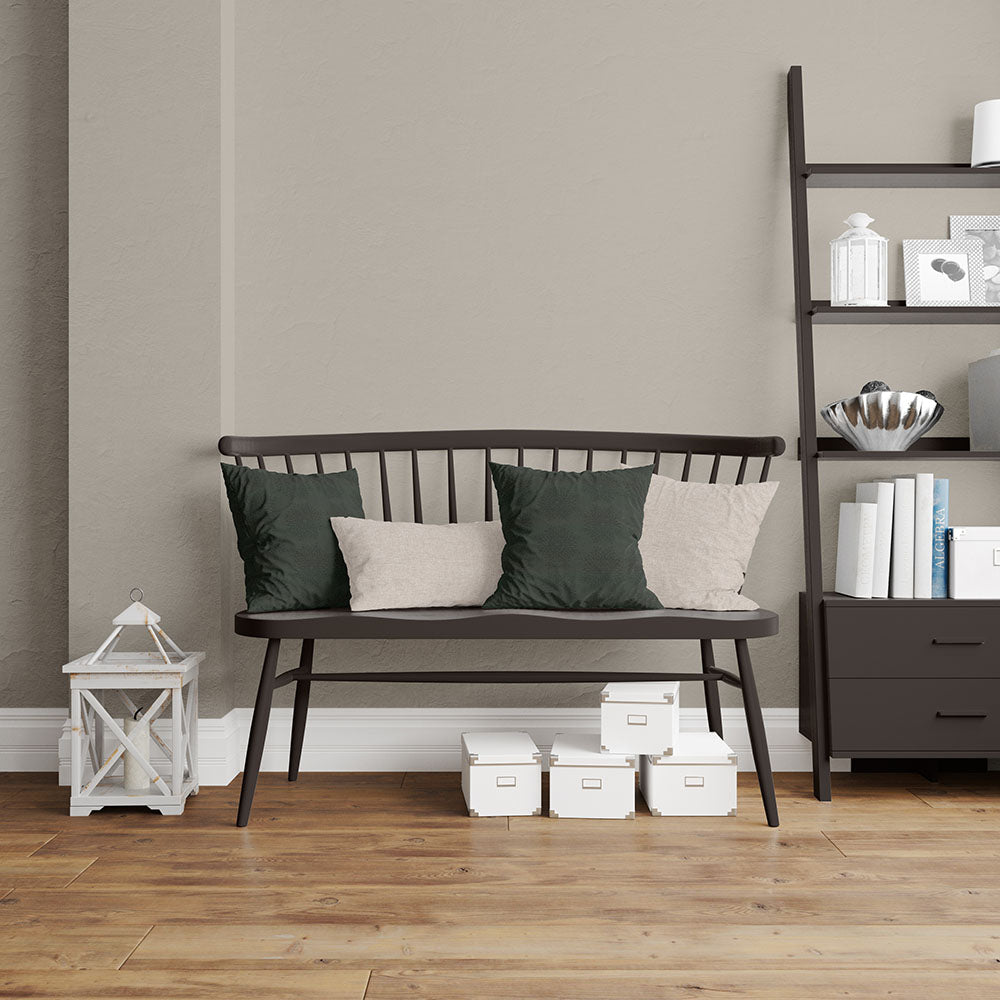 Dark brown wooden spindle-back bench with green and beige cushions on a warm wood floor beside a tall bookshelf.