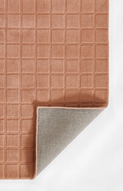Terracotta rug with square-grid texture; folded corner reveals gray backing, soft modern textile for living spaces.