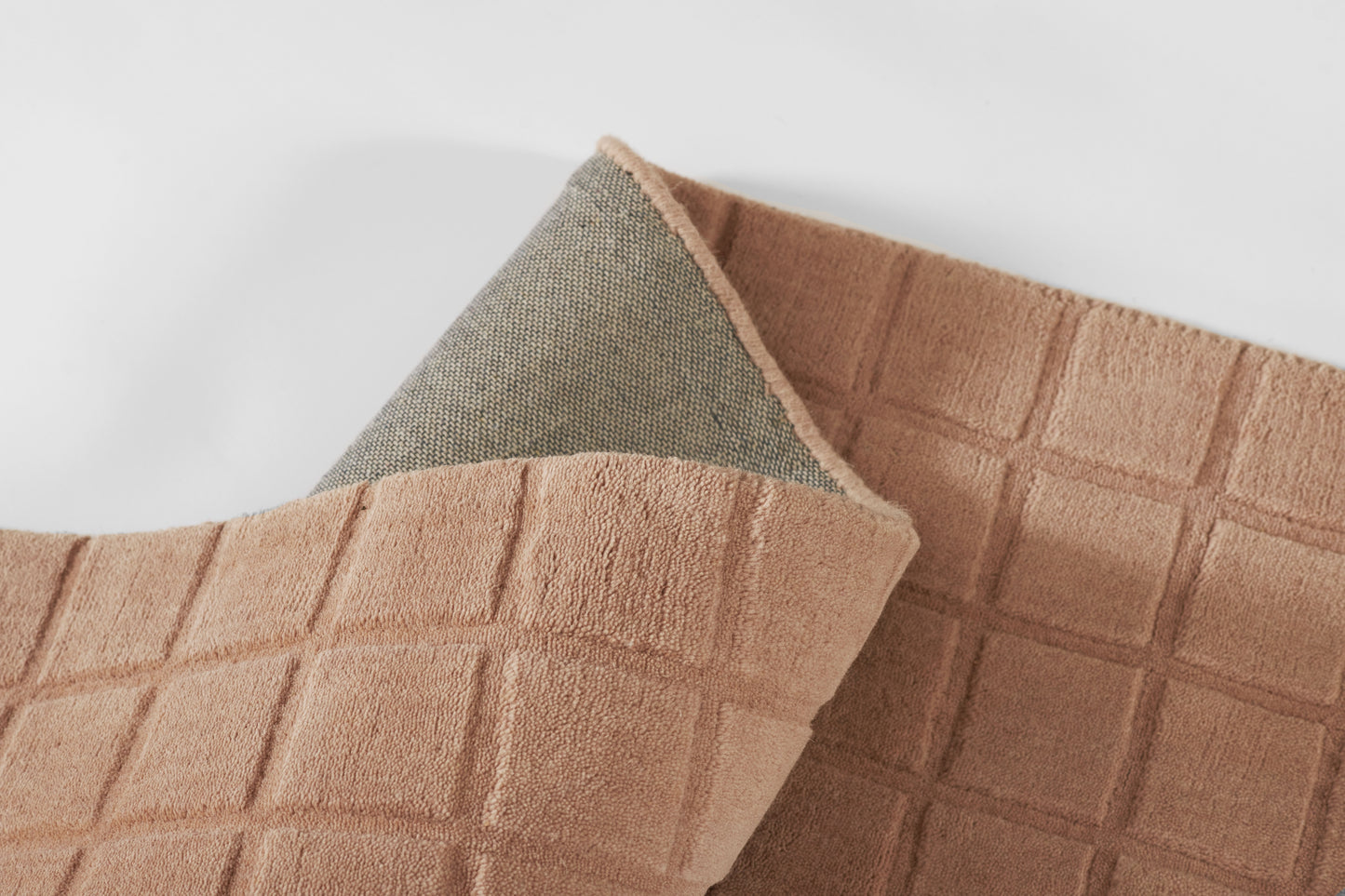 Peach-colored bath mat with a square grid texture; folded corner reveals grey underside, plush and soft.