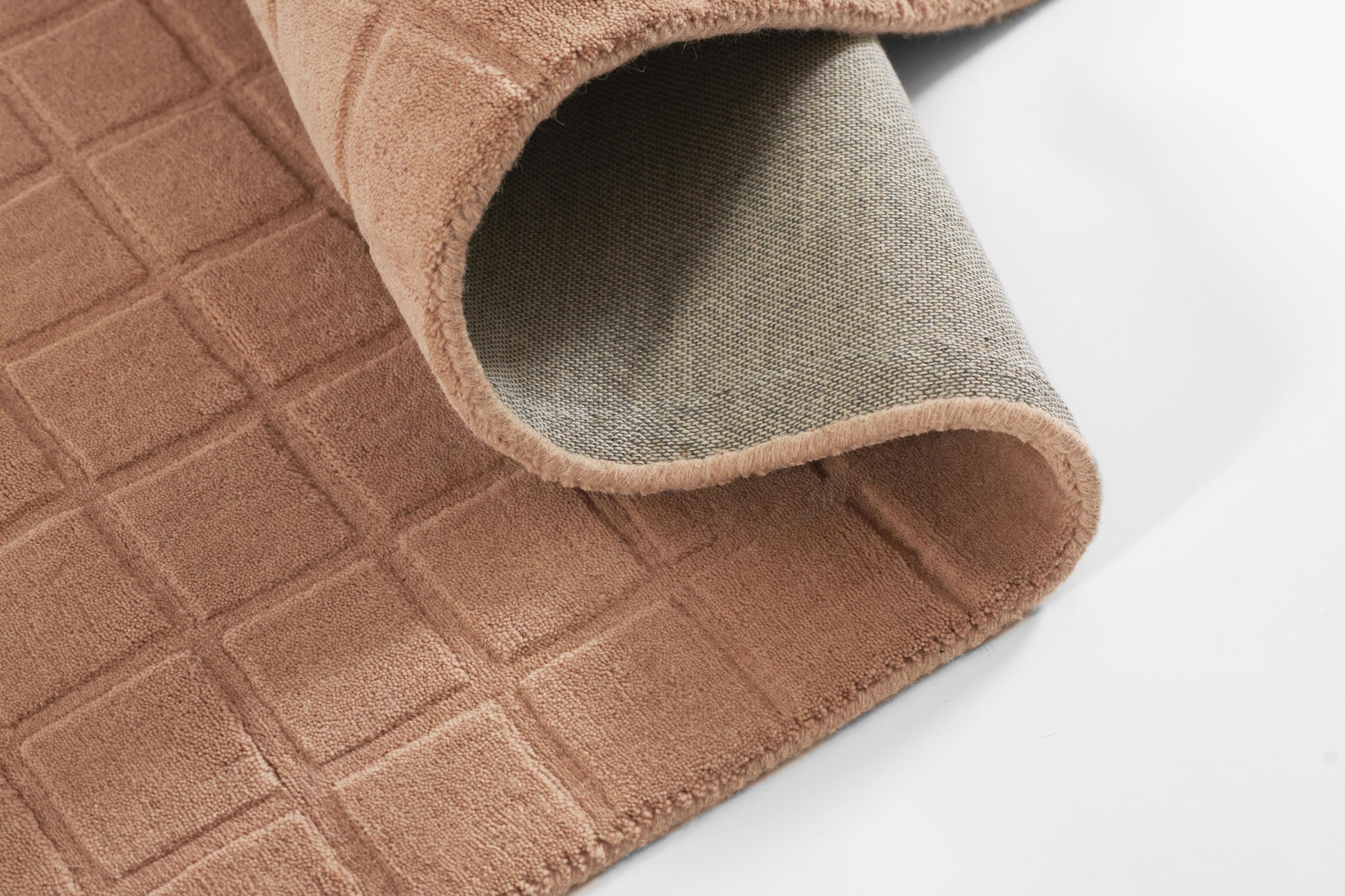 Beige-brown textured bath mat with a square grid pattern, folded to show a soft grey underside.