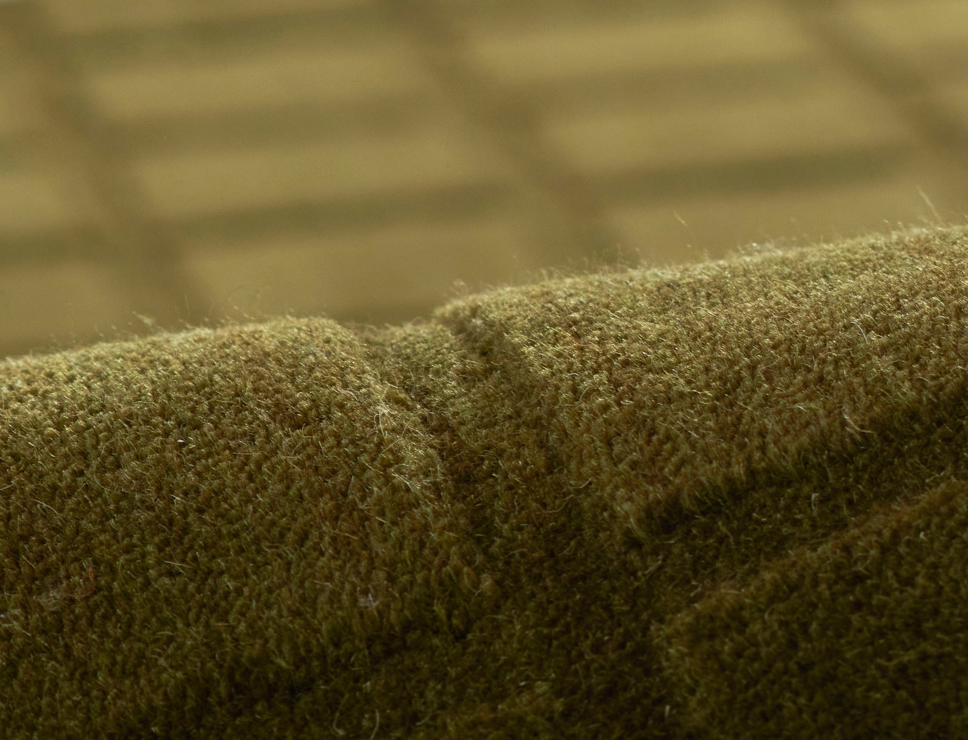 Olive-green plush fabric close-up with soft nap and seam, likely upholstery or cushion cover.