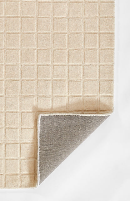 Beige grid-pattern rug with soft pile; folded corner shows gray underside, modern geometric style.