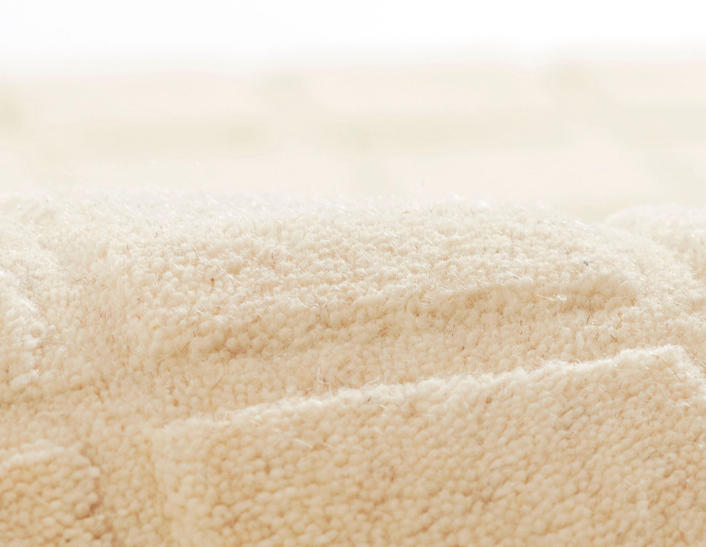 Beige plush terry towels with soft cotton loops, rolled and folded for a cozy bath set.