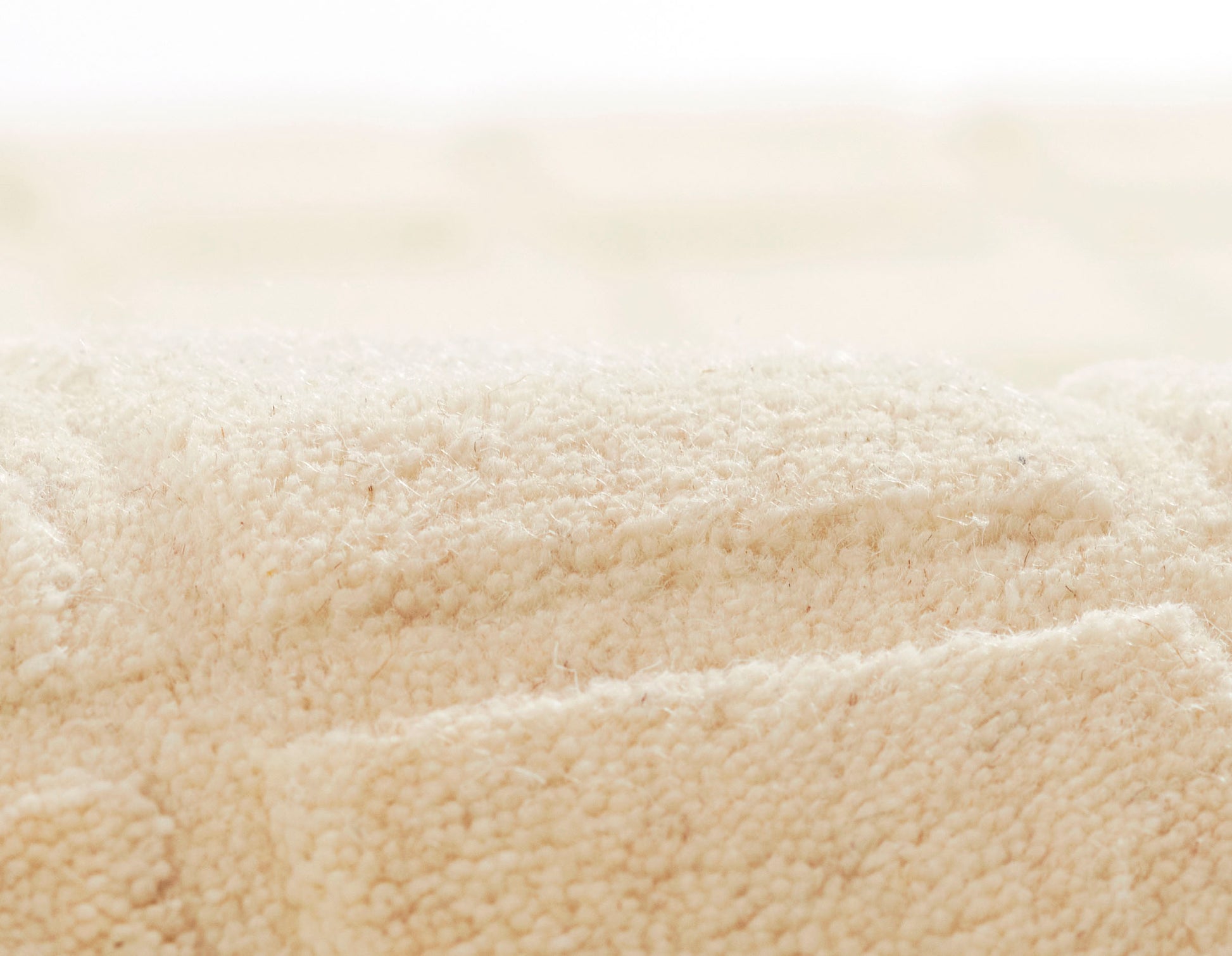 Beige plush terry towels with soft cotton loops, rolled and folded for a cozy bath set.