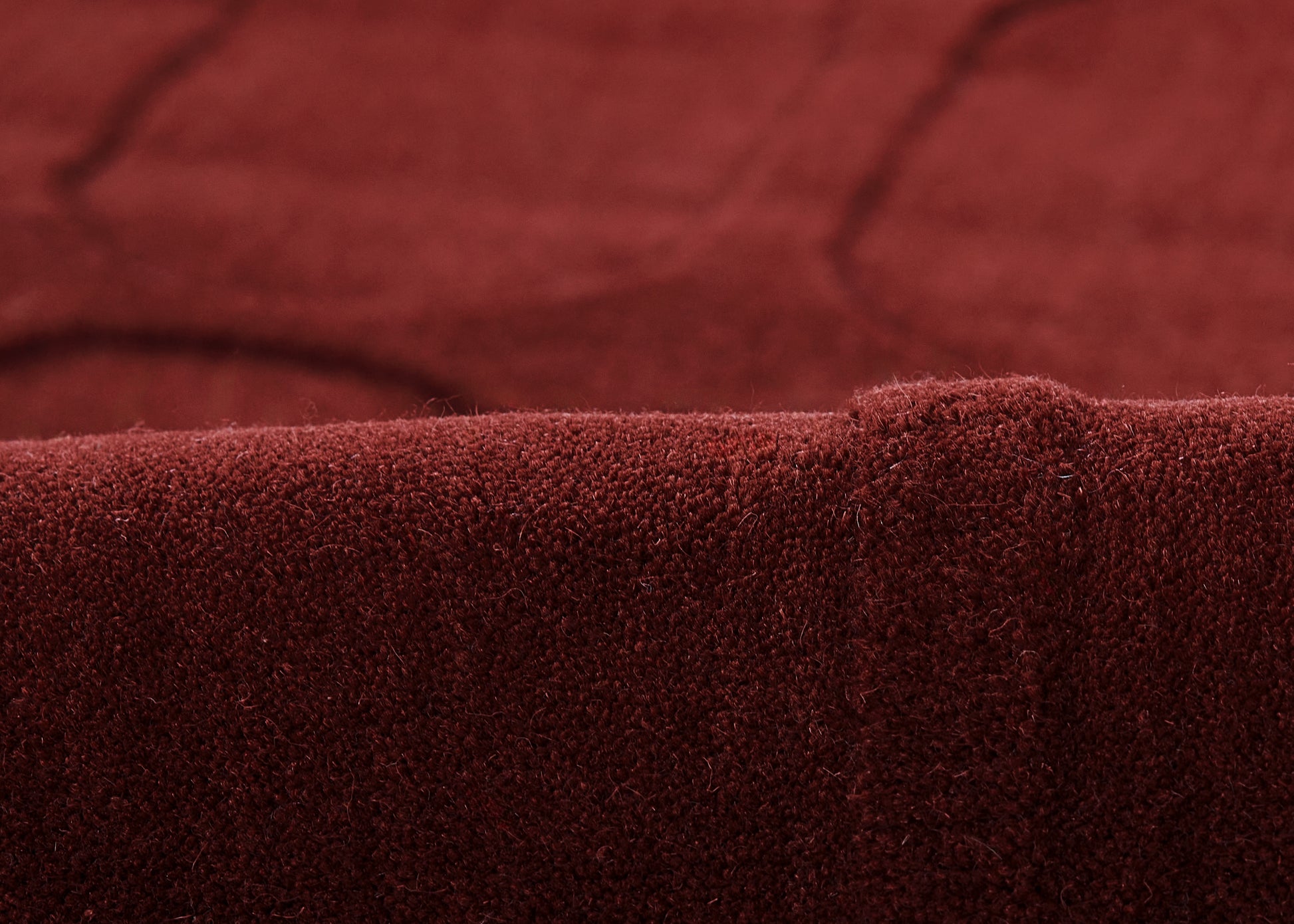 Close-up of burgundy velvet rug fabric with soft nap and folded edge.