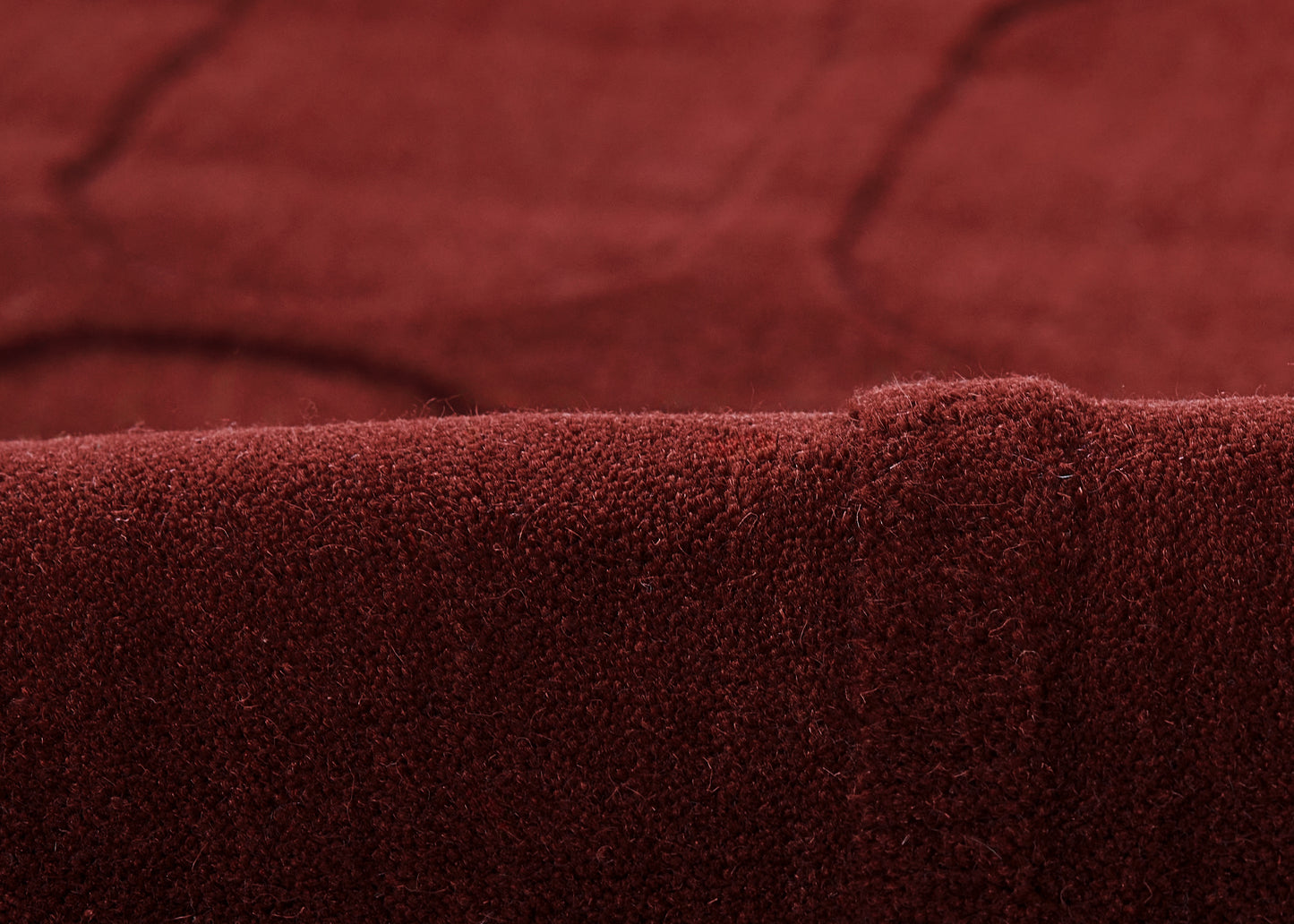 Deep burgundy velvet fabric close-up with a folded edge and plush nap, for upholstery or a throw.