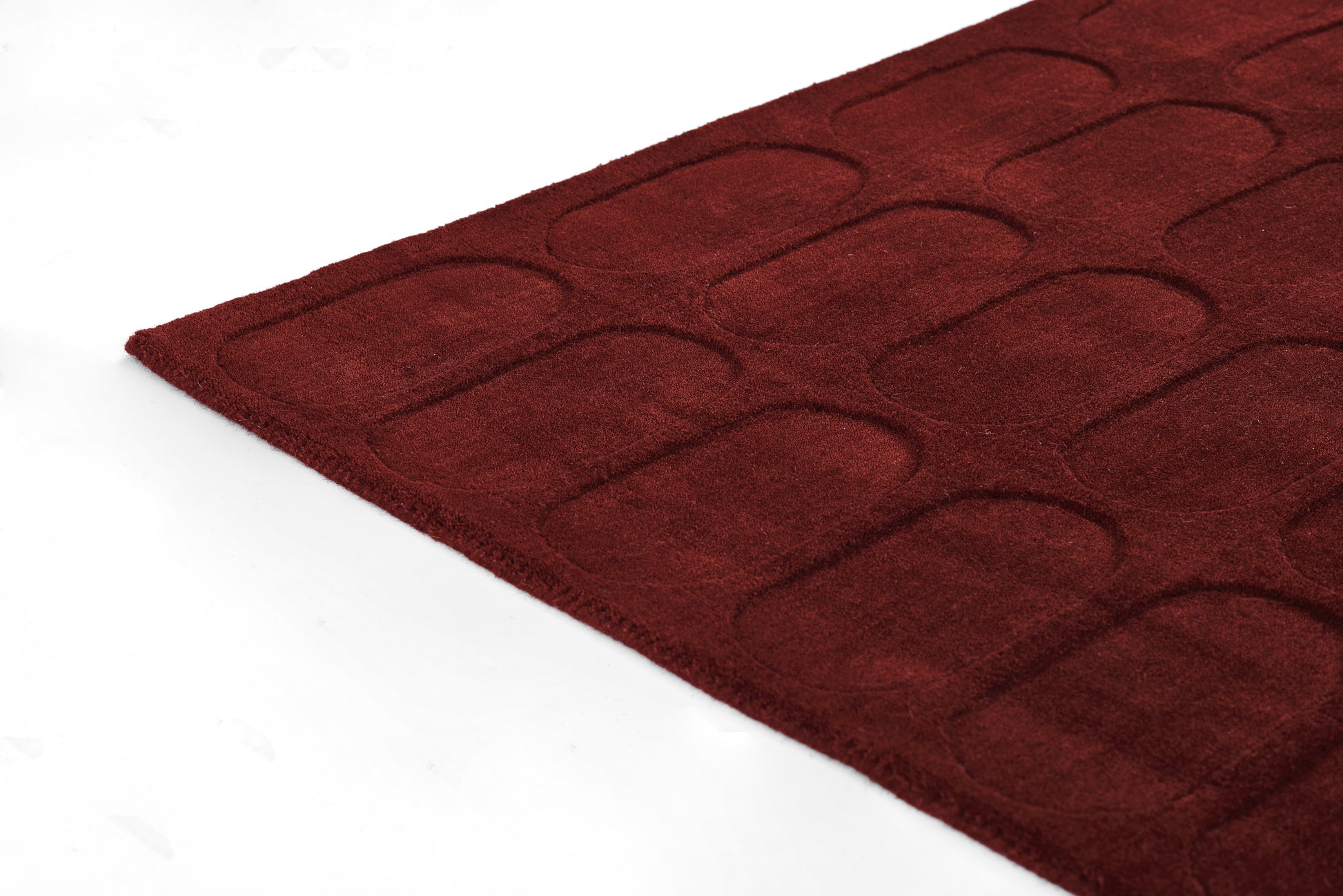 Deep burgundy tufted area rug with a rounded-rectangle pattern; plush low-pile, modern geometric design.