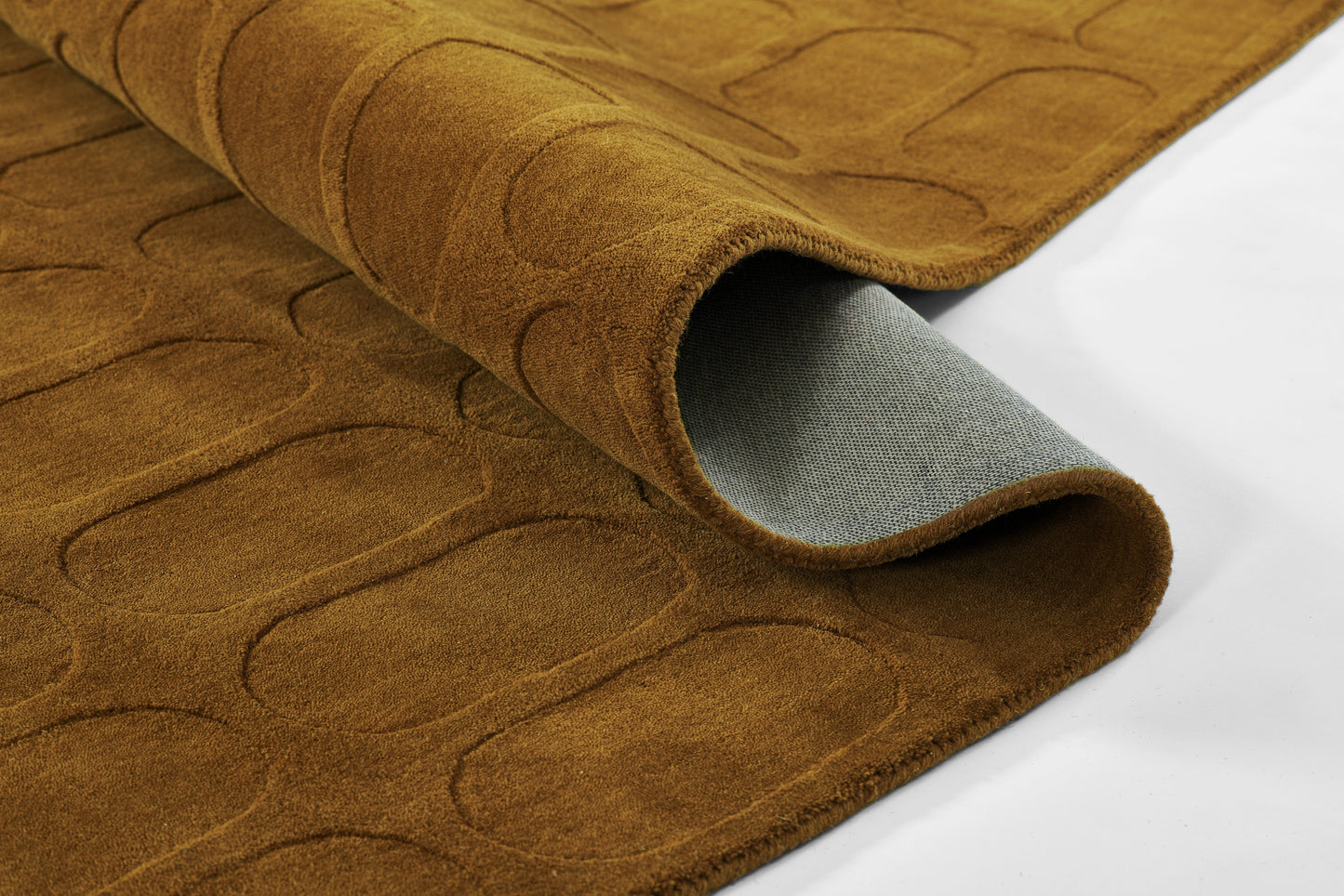 Brown suede-like rug with an oval quilted pattern, rolled to reveal gray backing; cozy, modern floor decor.