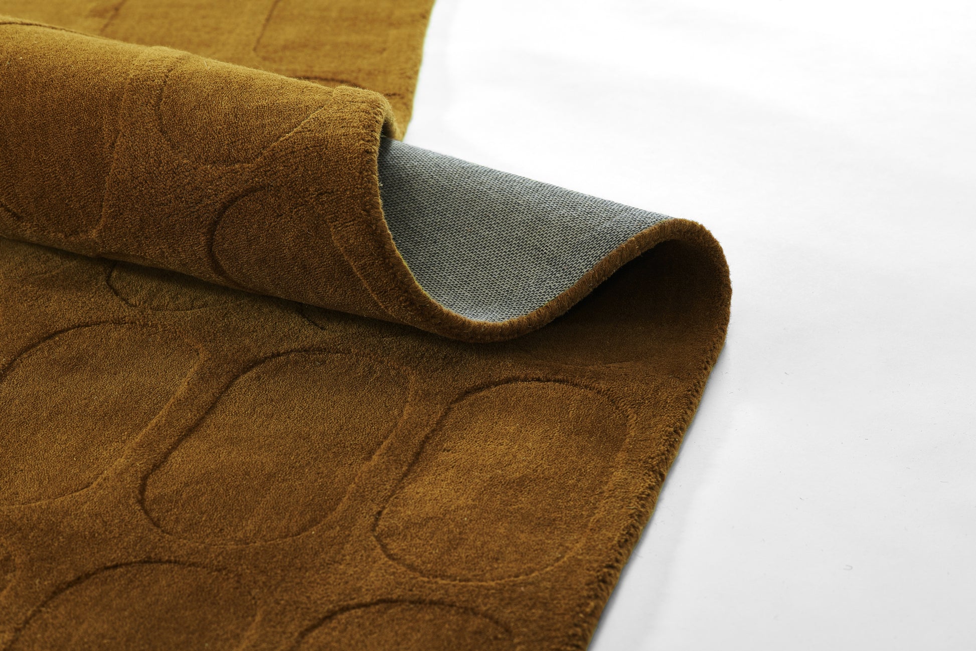 Brown suede-like rug sample with rounded-square embossed pattern; rolled to show grey underside.
