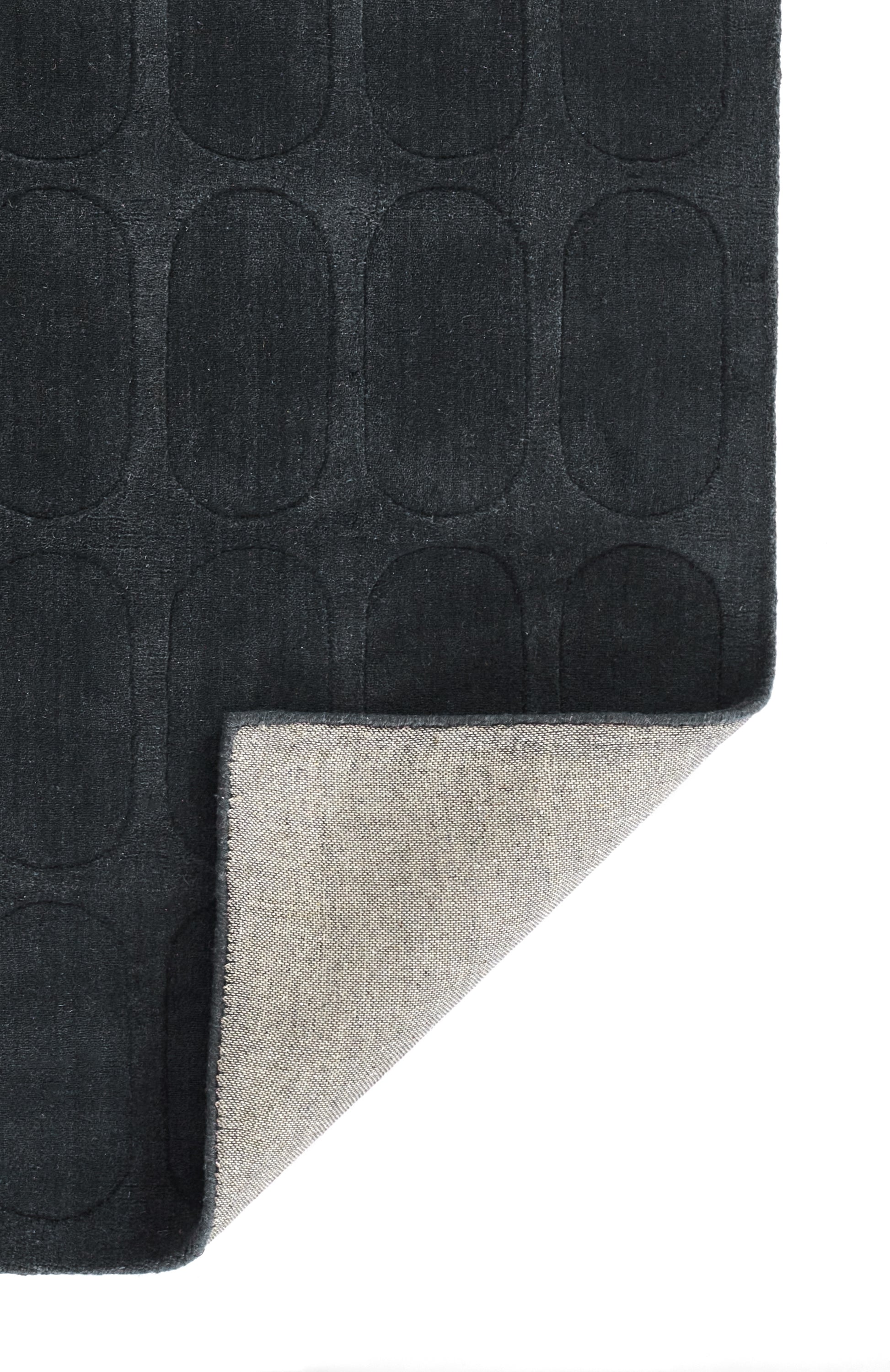 Charcoal rug with a grid of rounded-oval embossed shapes; soft texture, corner folded to reveal light beige backing.