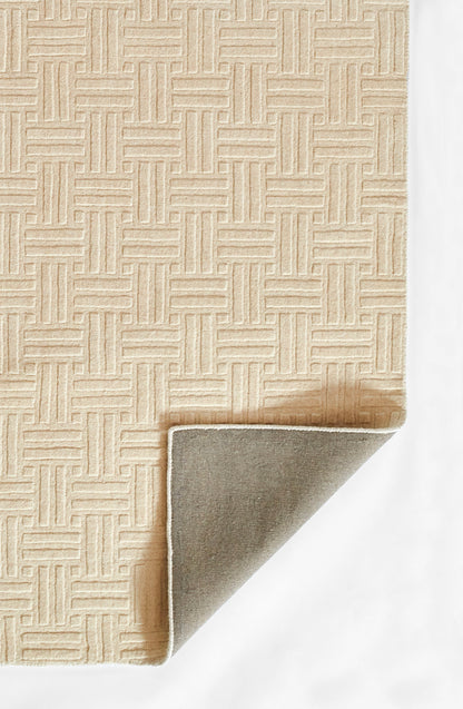 Beige textured rug with a geometric interlocking lattice pattern; folded corner reveals grey underside and white binding.