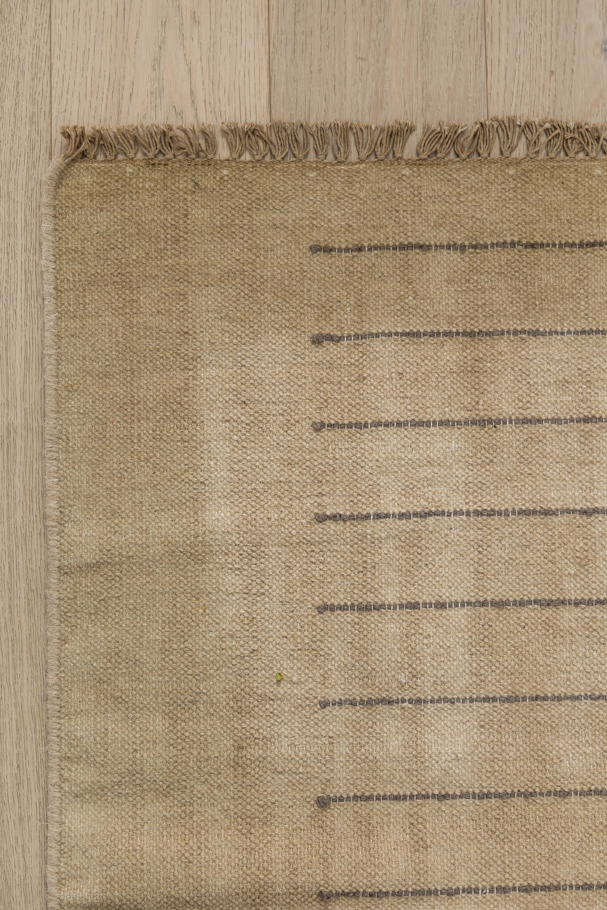 Beige jute rug with fringe along top edge and dark horizontal stripes; natural coastal woven style.