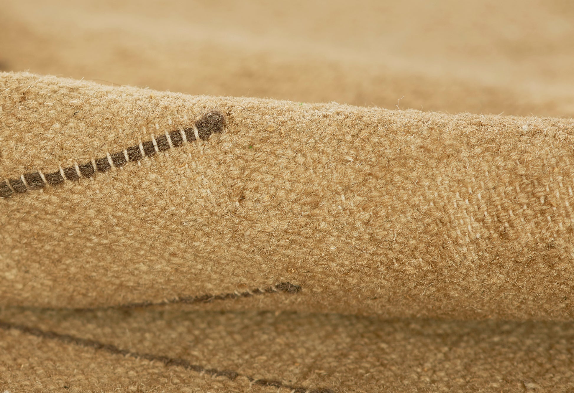 Coarse beige burlap fabric with a stitched seam & folded edge, showcasing natural jute texture.