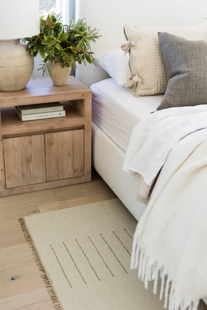Cozy living room corner with light wood side table, potted ivy, white sofa, beige and gray cushions, fringed cream throw.