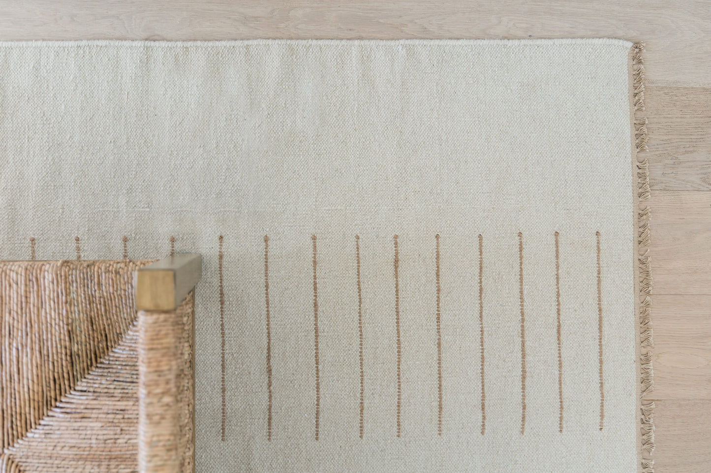 Beige woven rug with fringe edge on the right and subtle vertical stripe pattern; natural fiber, rustic chic home decor.