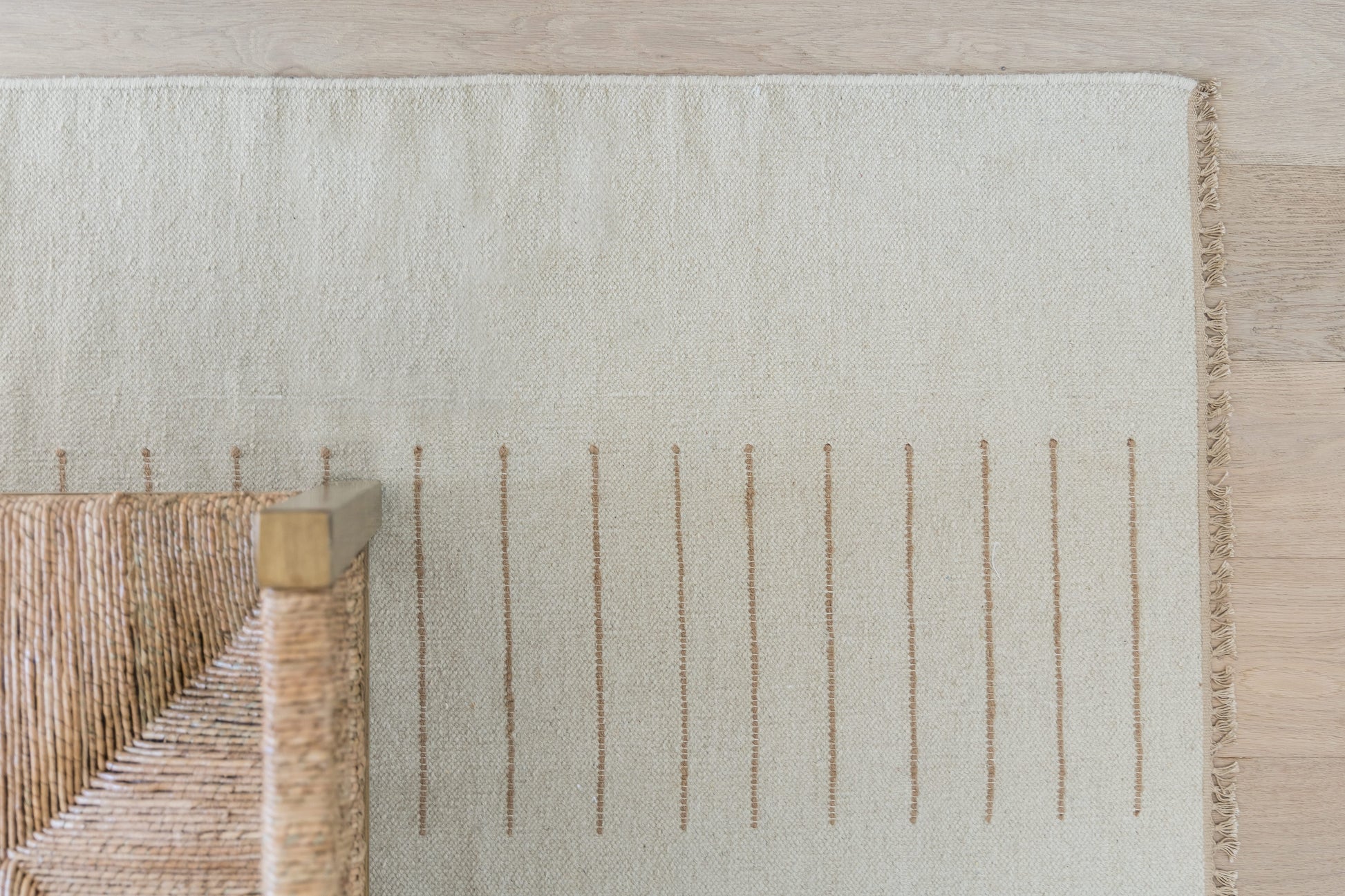 Beige woven rug with fringe edge on the right and subtle vertical stripe pattern; natural fiber, rustic chic home decor.