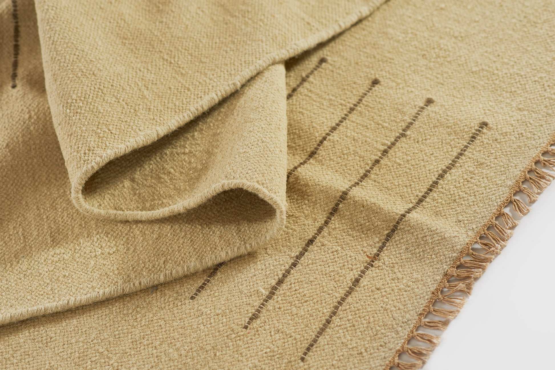 Beige woven rug with subtle brown stripes and tasseled fringe along one edge.
