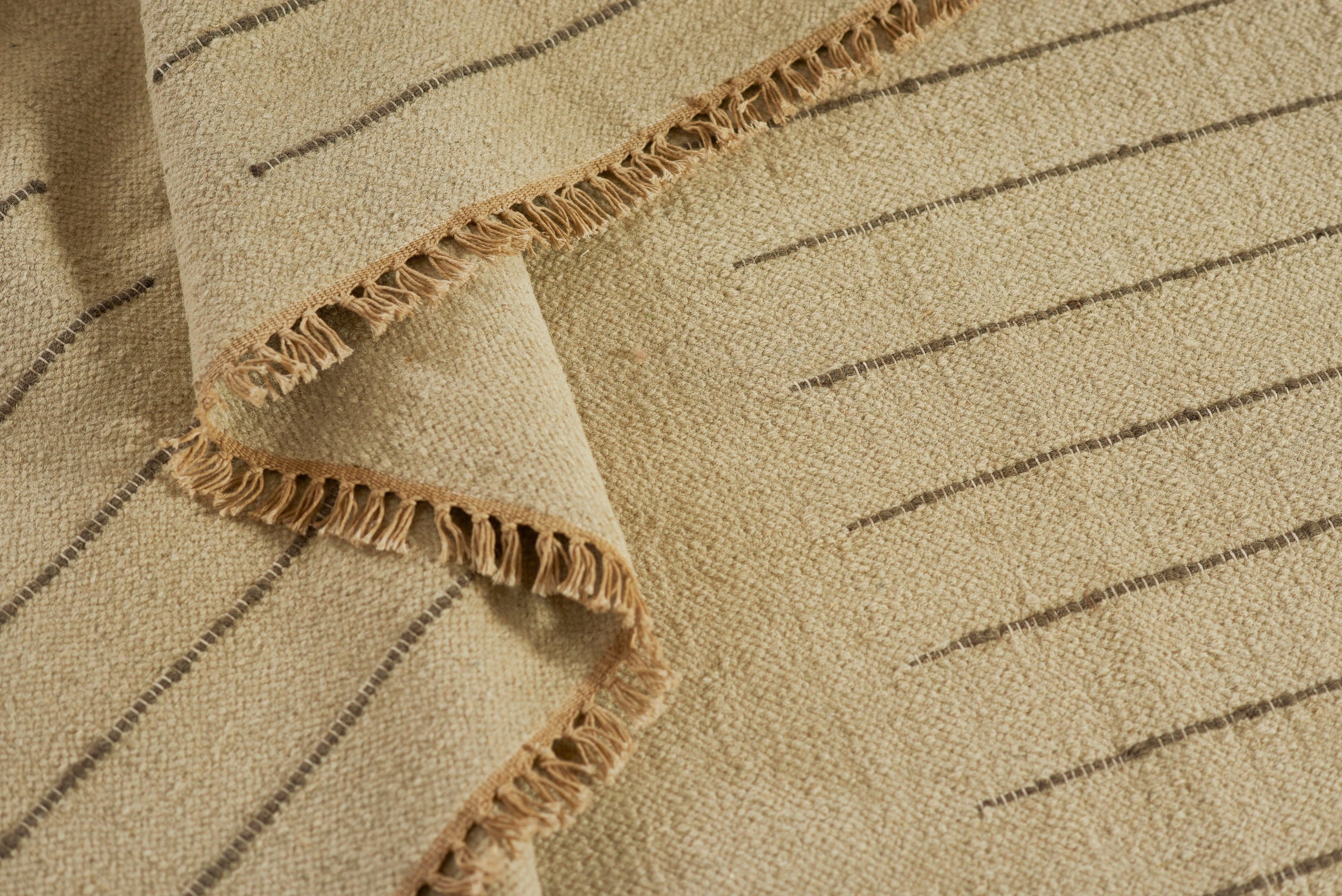 Beige woven rug with slim dark stripes and fringed edges.