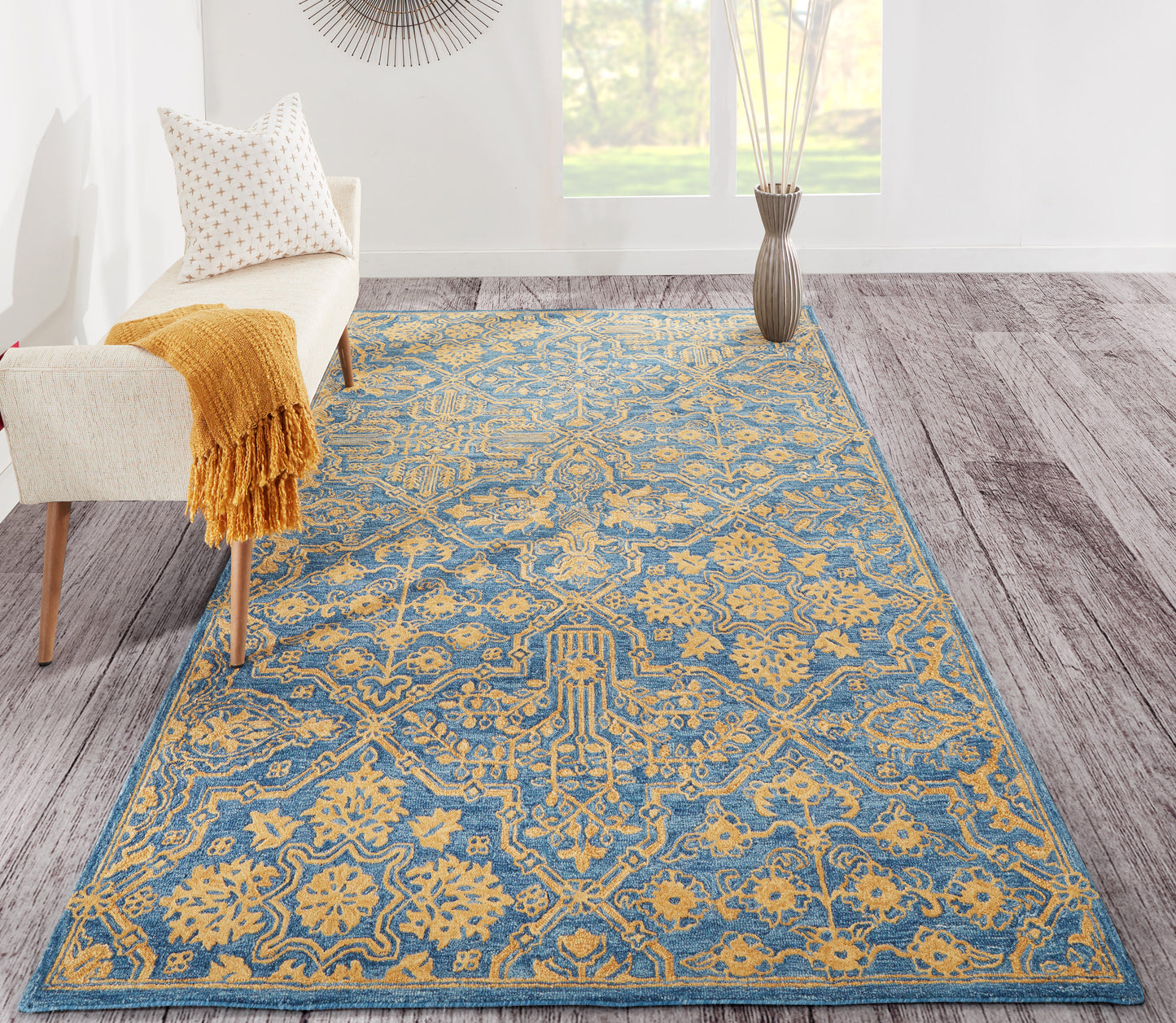 Blue and gold ornate woven area rug in a bright living room with a white armchair and mustard throw.