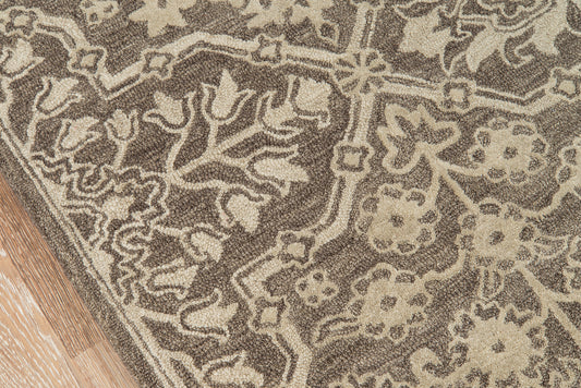 Close-up of a brown and beige patterned rug with floral/scroll motifs; wooden floor edge visible.