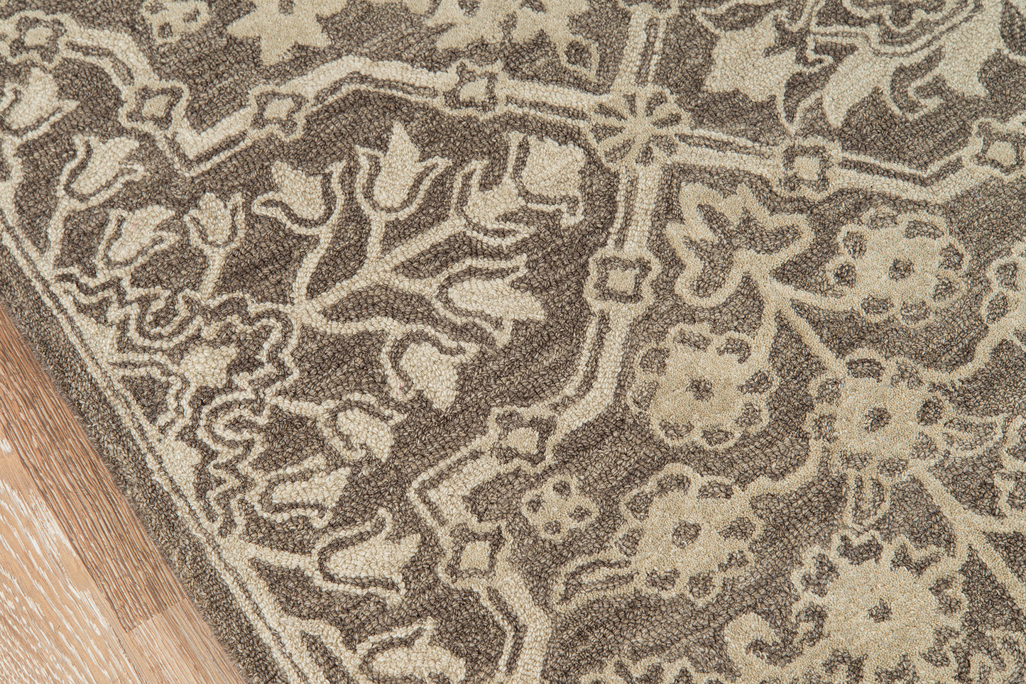 Brown and beige oriental-style rug with floral arabesque motifs, edge resting on a wooden floor.