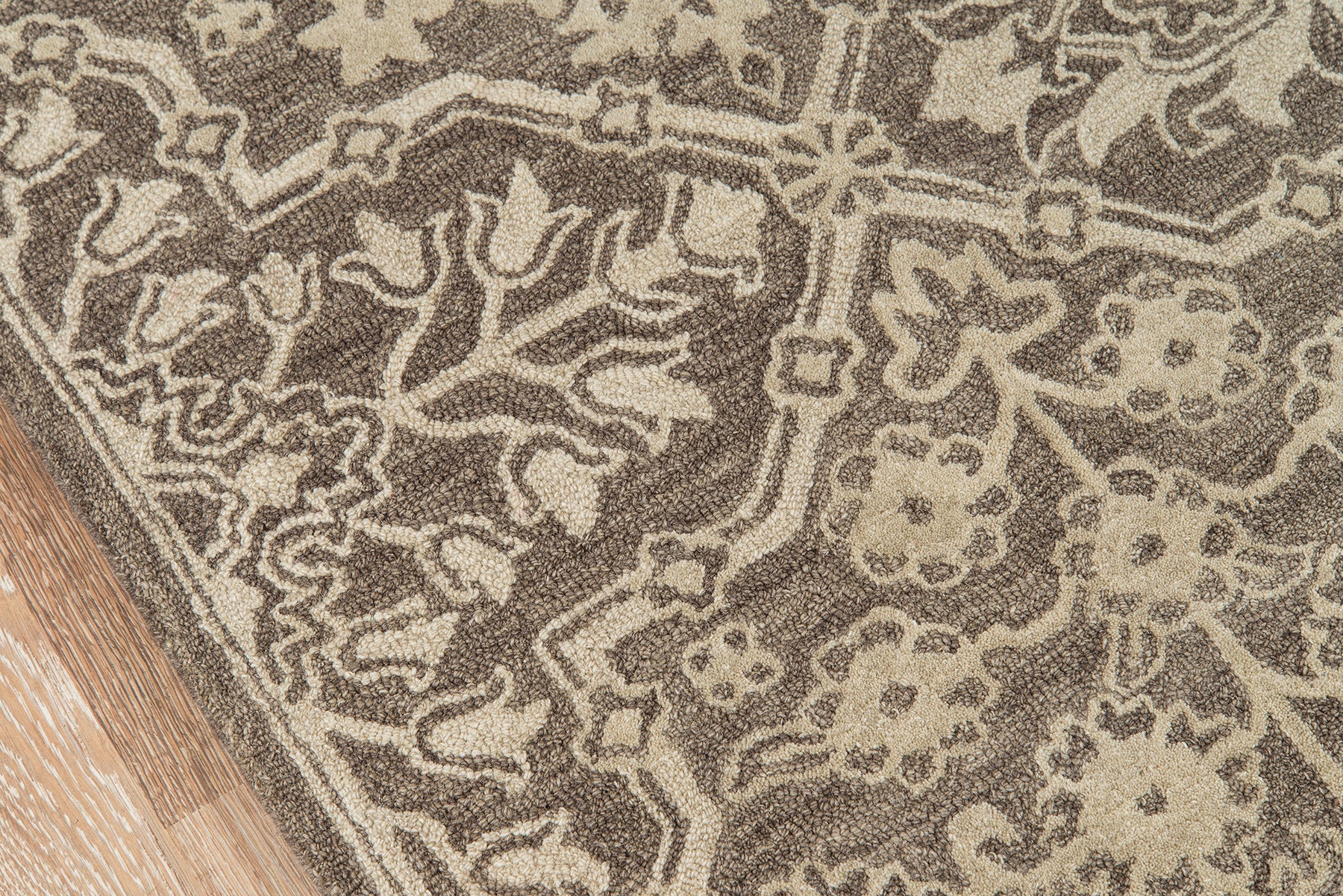 Brown and beige oriental-style rug with floral arabesque motifs, edge resting on a wooden floor.
