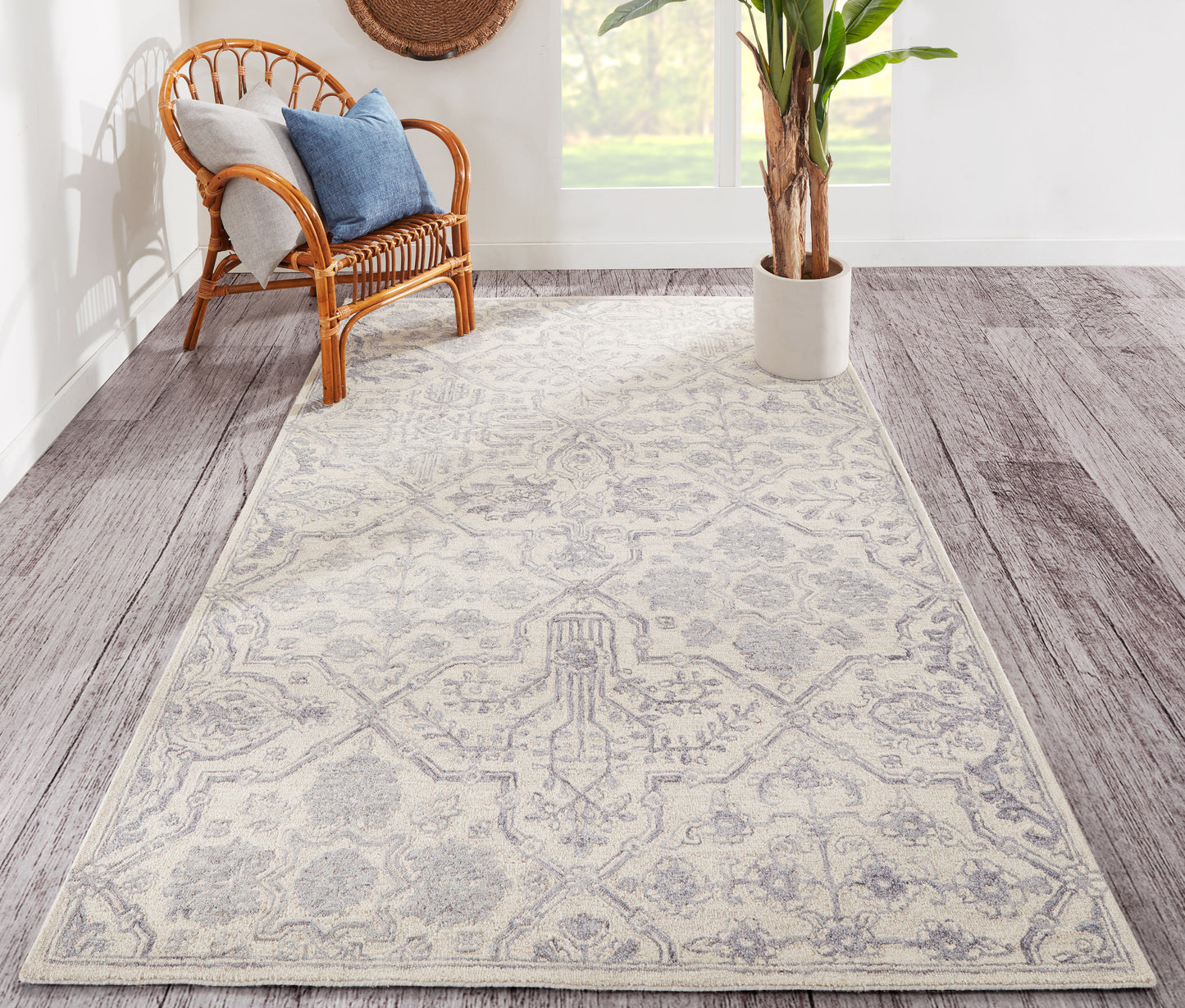 Light gray patterned area rug on wood floor; wicker chair with blue cushions and a potted plant in a bright room.