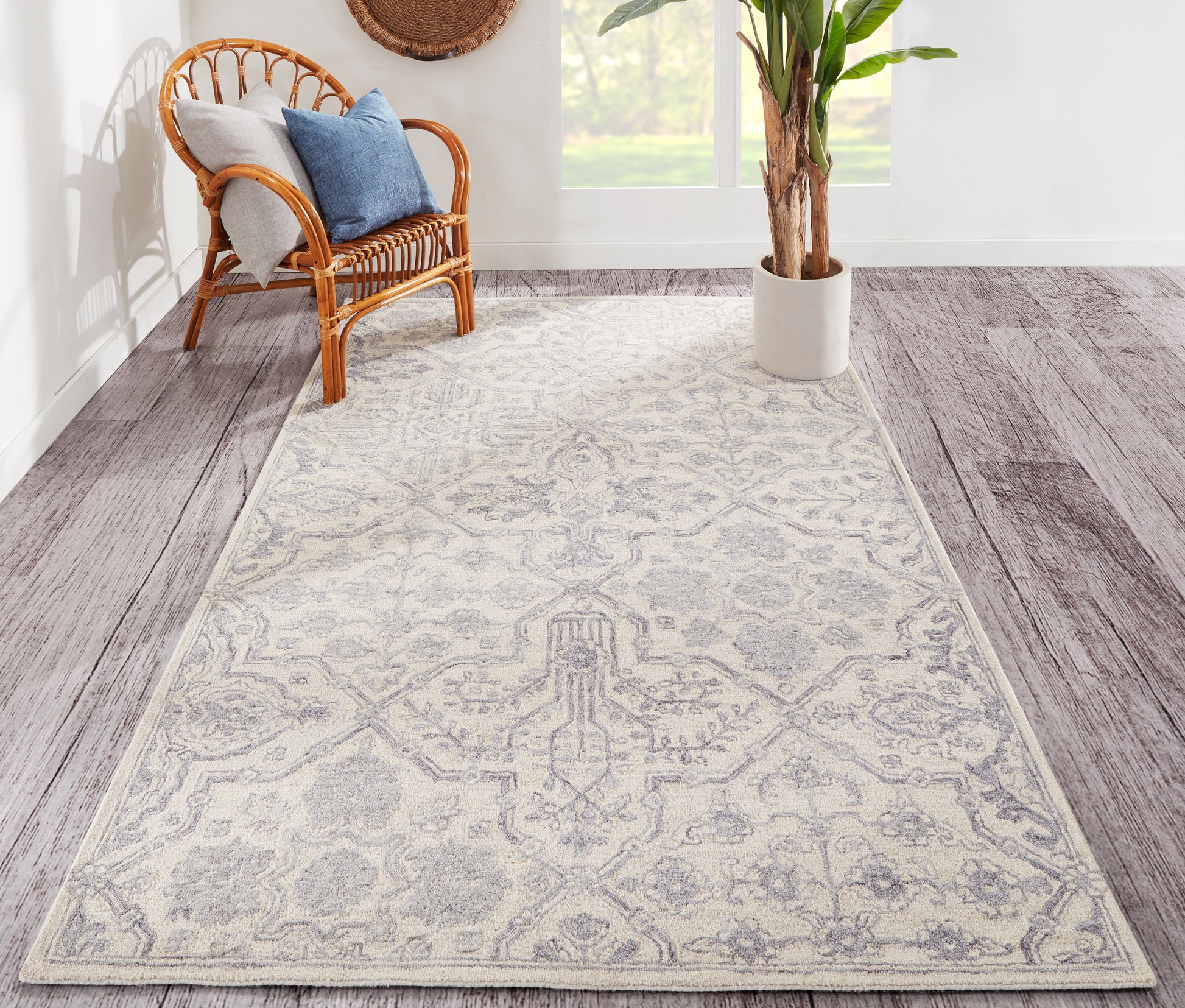 Gray patterned rug with ivory motifs on wood floor; wicker chair with blue cushions and a potted plant.