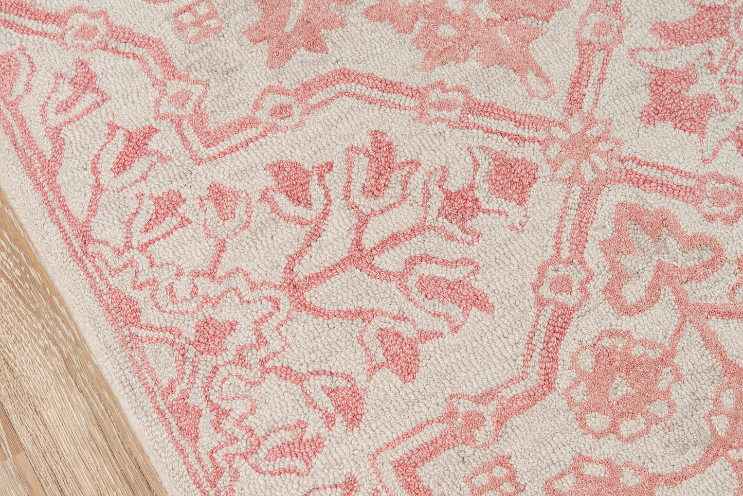Pink floral patterned rug on beige background with wood flooring edge.
