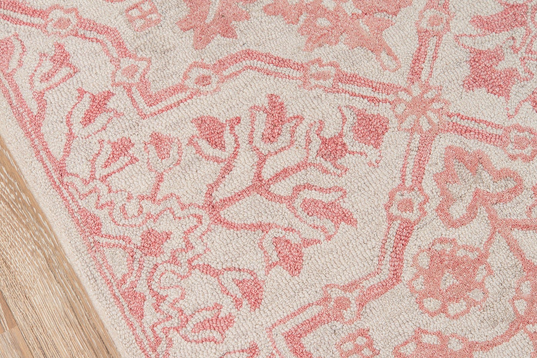 Pink floral patterned rug on beige background with wood flooring edge.