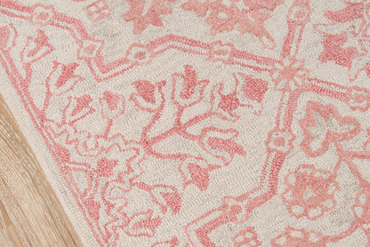 Pink floral patterned rug on beige background with wood flooring edge.