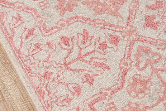 Pink and cream patterned rug with floral and vine motifs on light beige; wooden floor edge visible.