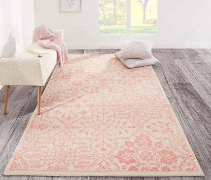 Pink 8' x 10' area rug with a pale peach ornate floral-medallion pattern, placed in a bright living room with a sofa and cushions.