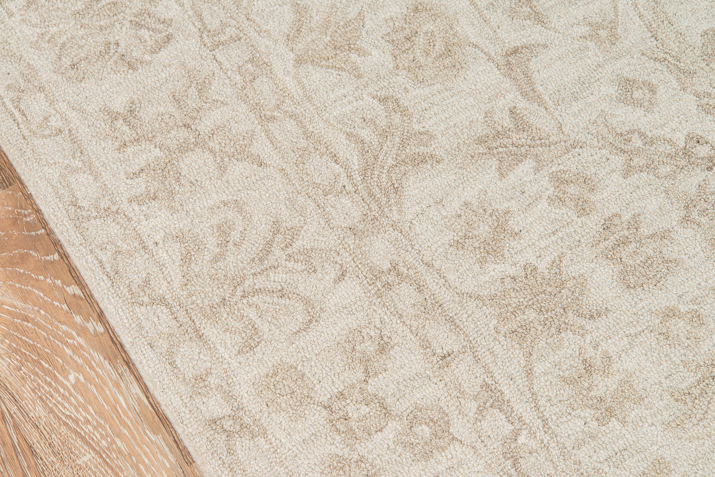 Beige patterned area rug with subtle floral damask design beside a wooden floor edge.