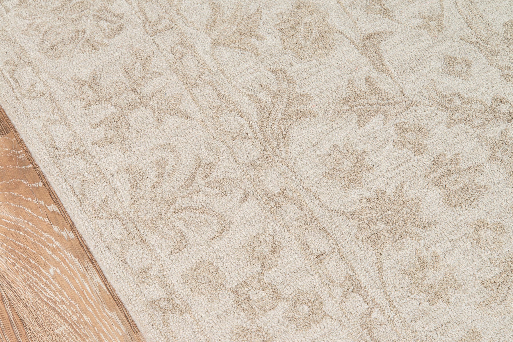 Beige patterned area rug with subtle floral damask design beside a wooden floor edge.
