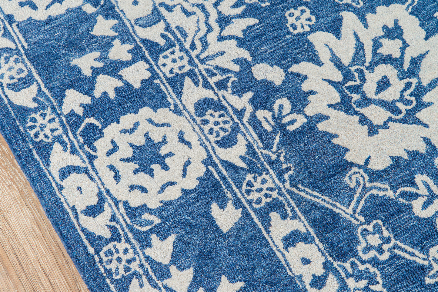 Blue and white floral patterned rug with decorative borders on a wooden floor.